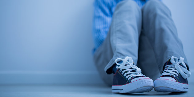 Sad boy in sneakers with asperger's syndrome sits alone in his room