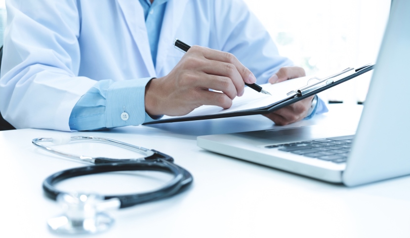 Doctor working with laptop computer and writing on paperwork. Hospital background.