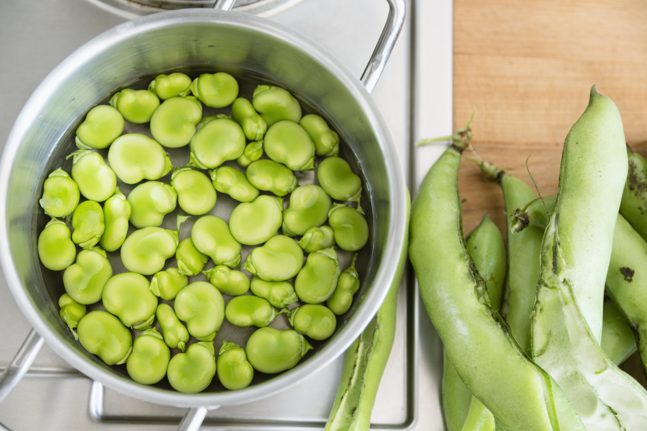 Broad beans, fresh from the garden, are cooking in a pot in the kitchen