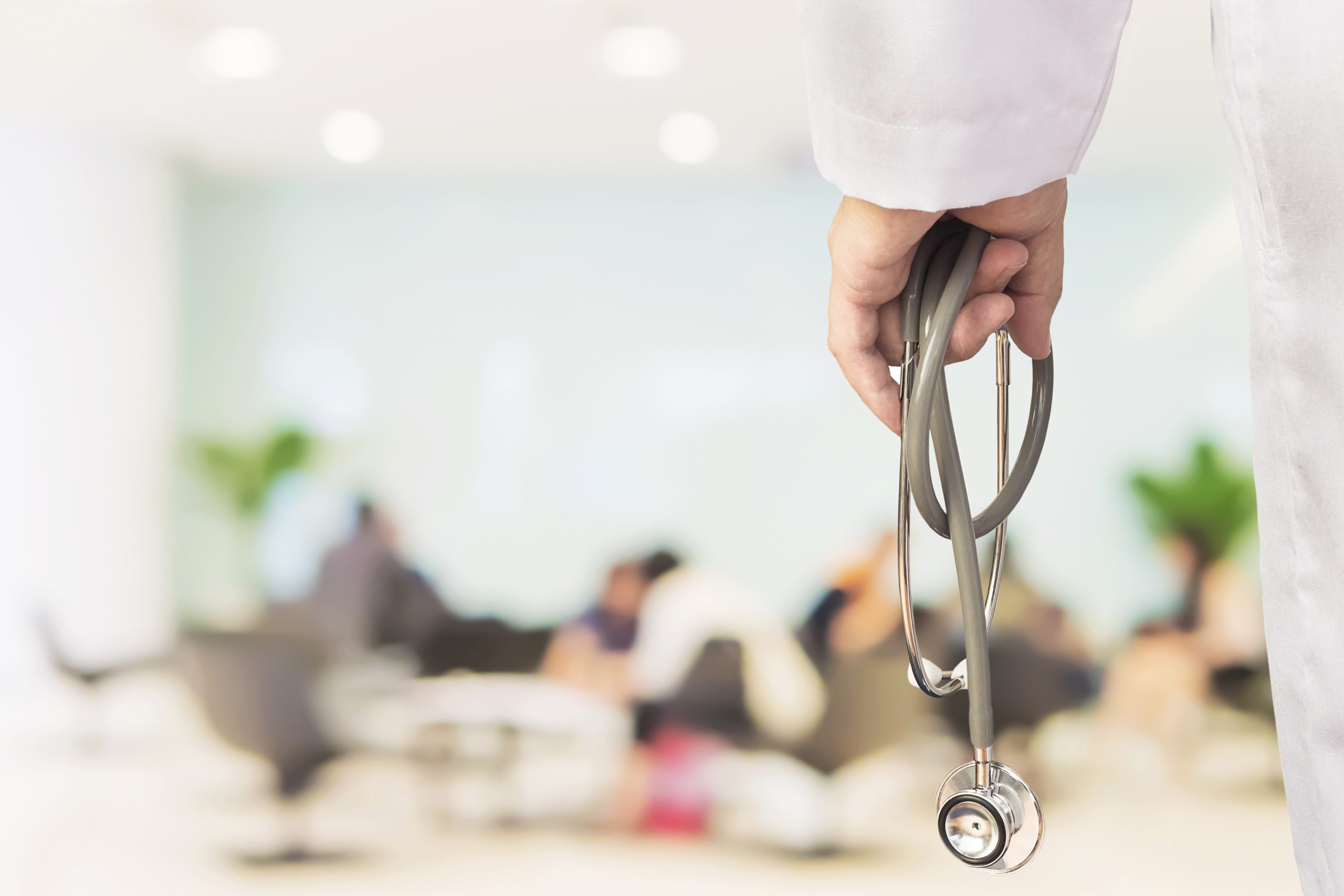 Doctor is going to examine his patient using his stethoscope over sitting people in modern hospital background