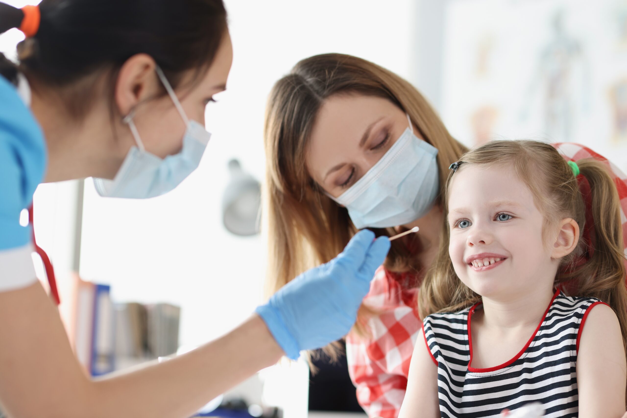 Portrait of doctor collects biological material from child saliva, coronavirus nasal swab test for kids. Little girl patient in hospital. Virus outbreak, analysis, checkup, medicine, health concept